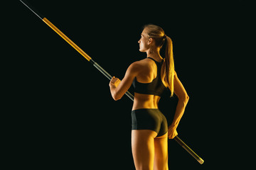 Power and beauty. Professional female pole vaulter training on black studio background in neon...