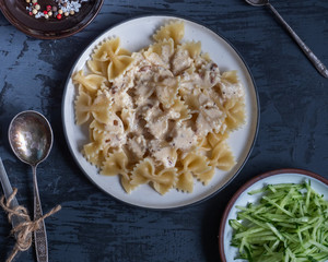 Breakfast of pasta and fresh cucumber salad in round plates on a gray background, forks and spoons, seasonings on a small saucer, TOP VIEW