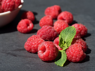 Fresh raspberries in bowl on a stone stand on a dark stone background.