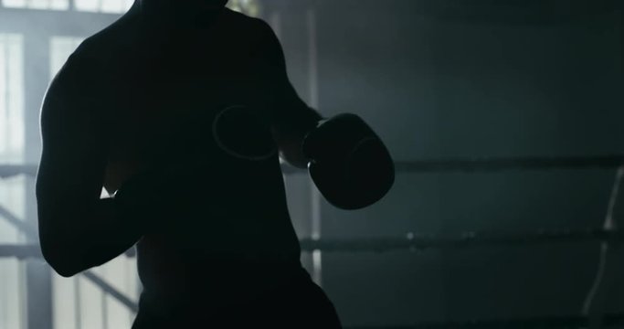 Cinematic slow motion shot of two professional young muscular shirtless male boxers are fighting and embracing after in a boxing ring.