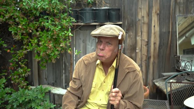 Hysterical and deranged old man holding cane in a threatening manner and making crazy faces, including pouting.