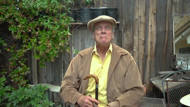 Demented old man with cane making crazy face and holding his hands up and spread out like claws. Holding cigar in one hand.