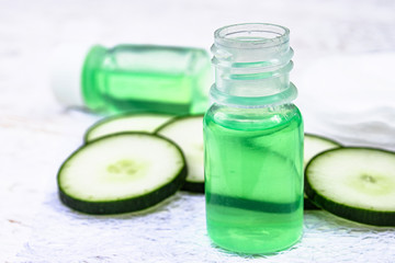 Liquid cosmetics skin care in a bottle and green cucumber with a slice of cucumber on a white wooden table. Natural extract from cucumber.