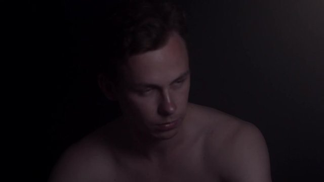 Young naked paranoid guy in the darkness with headache feeling anxious.