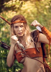 Beautiful girl archer with long blond hair with bow and arrowson a back holding two steel knifes...