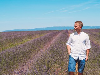 Naklejka na ściany i meble A blond man in a white cotton shirt stands in a lavender field in Provence in France, Valensol