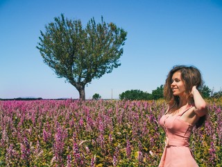 Brunette girl with long hair in a delicate pink dress rustic stands in a lavender field in Provence in France, Valensol, heart-shaped tree