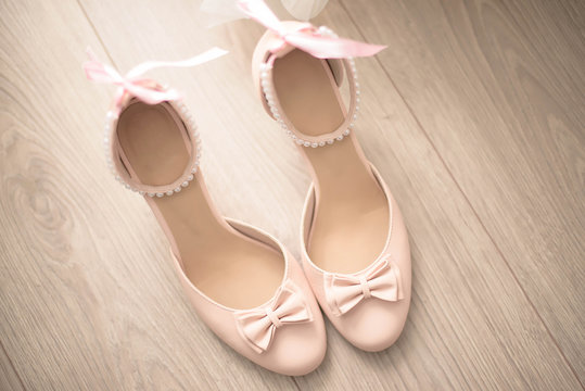 Top view of a beige leather chunky mid heel women shoes with delicate bow an pearls strap against a wooden background. Elegant women footwear for formal occasion or day-to-day wear.