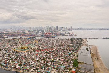 Port in Manila, Philippines. Sea port with cargo cranes. Cityscape with poor areas and business center in the distance, view from above. Asian metropolis.