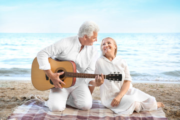 Fototapeta na wymiar Mature man playing guitar for his wife at sea resort