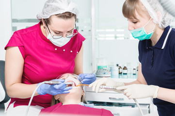 Female dentist and nurse doing professional care and tooth brushing of a young patient in a dental office