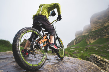 Rear view wide angle of a man on a mountain bike stands on a rocky terrain and looks at a rock. The concept of a mountain bike and mtb downhill