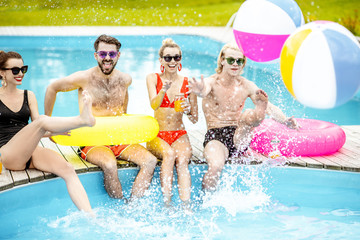 Group of a happy friends having fun, playing with inflatable balls and rings on the water pool outdoors during the summer time