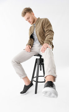 Stylish Young Man Sitting On Stool Against White Background