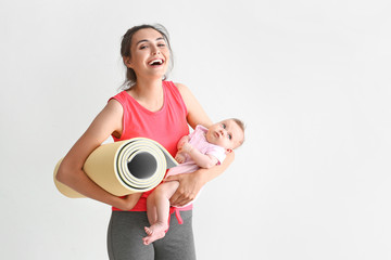 Mother with yoga mat and cute little baby on white background