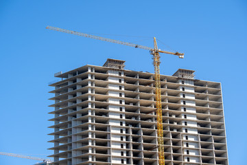 Fototapeta premium Construction of a high-rise building with a crane. The construction crane and the building against the blue sky.