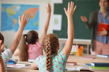 Cute little pupils raising hands during lesson in classroom