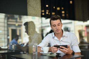 Young fashion man / hipster drinking espresso coffee in the city cafe during lunch time and working on tablet computer