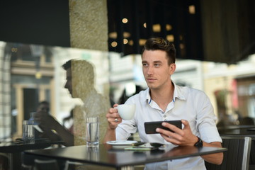 Young fashion man / hipster drinking espresso coffee in the city cafe during lunch time and working on tablet computer