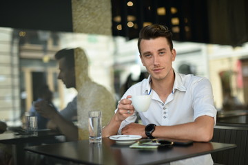 Young fashion man / hipster drinking espresso coffee in the city cafe during lunch time and working on tablet computer