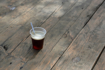 A plastic glass with a spoon and coffee is on the table of boards