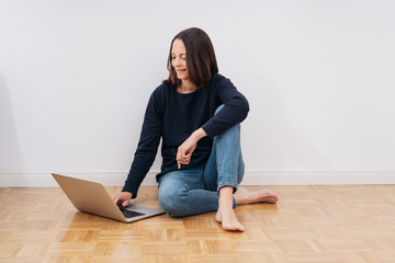 frau sitzt in einer leeren wohnung auf dem boden mit laptop