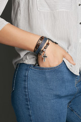 Cropped top and bottom photo of a woman with a bracelet on her arm. The model on a gray background is dressed in a light striped shirt and jeans. You can see a multi-layer bracelet made from leather a