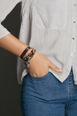Cropped top and bottom photo of a woman with a bracelet on her arm. The model on a gray background is dressed in a light striped shirt and jeans. You can see a multi-layer bracelet made from leather a