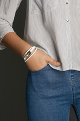 Cropped top and bottom photo of a woman with a bracelet on her arm. The model on a gray background is dressed in a light striped shirt and jeans. You can see a multi-layer bracelet made from a leather