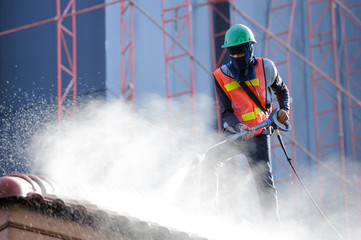 Worker in safety vest cleaning roof tiles with high pressure cleaning machine