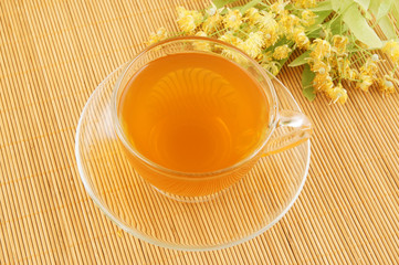 Glass cup of lime tea with lime blossoms on bamboo background