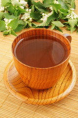 Wooden cup of nettle tea on bamboo mat