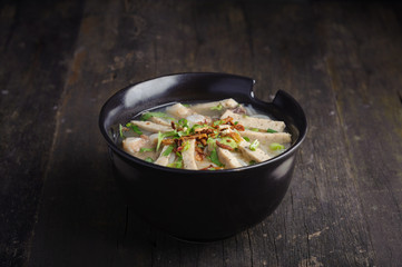 Paste of rice flour with scallion, coriander, deep fried garlic and porks on top in black porcelain bowl. Studio shot