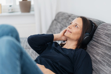 frau liegt zuhause auf dem sofa und hört musik