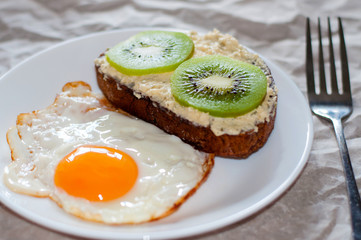 Delicious and healthy breakfast. Fried eggs and kiwi sandwich on white plate