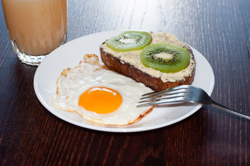 Healthy, tasty breakfast, juice, wholemeal bread sandwich with kiwi and a fried egg on a white plate, on a wooden table