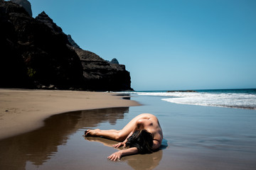 young lonely nude woman laying crouched on pristine beach as a metaphor for loneliness depression...