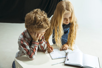 Boy and girl preparing for school after a long summer break. Back to school. Little caucasian models making homework together on studio background. Childhood, education, holidays or homework concept.