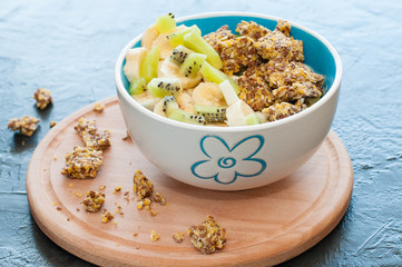 Granola, kiwi, banana and yogurt in a bowl on a wooden stand, gray background, view from the side. Fitness diet for weight loss