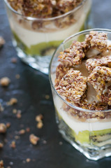 Greek yogurt, granola, banana and kiwi. Desserts in glass cups on dark background, side view from the top. Concept body and healthy food