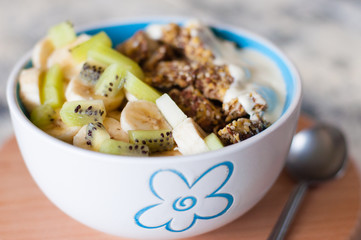 Greek yogurt, granola, kiwi and banana in a bowl on a gray concrete background, wooden tray, close-up. Fitness diet for weight loss, proper and tasty food