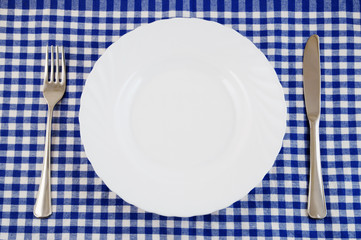 Top view of white plate, fork and knife on tablecloth