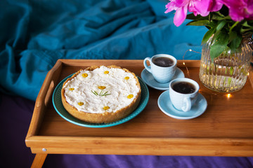 Breakfast in bed. Beautiful light from the window-peonies, cheesecake and two cups of coffee on a wooden tray.