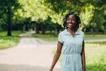 Portrait of a African beauty smiling young black woman in a park with sunlight flare and copy space