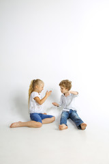 Boy and girl, best friends or brother and sister having fun. Little caucasian models in jeans playing together on white studio background. Childhood, education, holidays or homework concept.