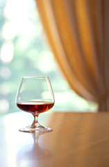 Glass of Cognac opposite curtain and window 