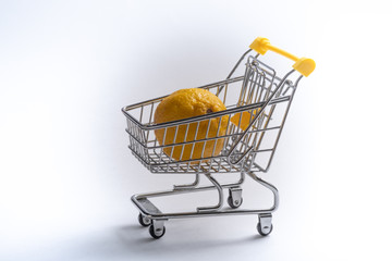 Close-up of shopping carts on white background..Trolley and limon , Sale concept.. Isolated over white background in a cart lies a yellow citrus.