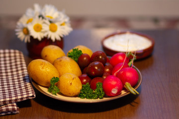 Cooked  upeeled potato, dark small tomato, radish, white sauce and bouquet of camomiles in vase on wooden table