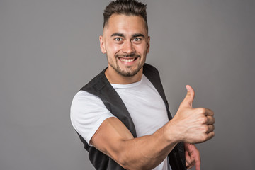 young, sporty, inflated, cute, sexy, emotional man, semi-naked, in a vest from a suit and a white T-shirt, shows emotional gestures with hands and facial expression on a gray background