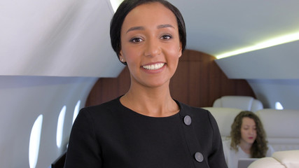 Fototapeta premium Biracial businesswoman in private jet. Well dressed, confident female african entrepreneur smiling inside of business airplane cabin.